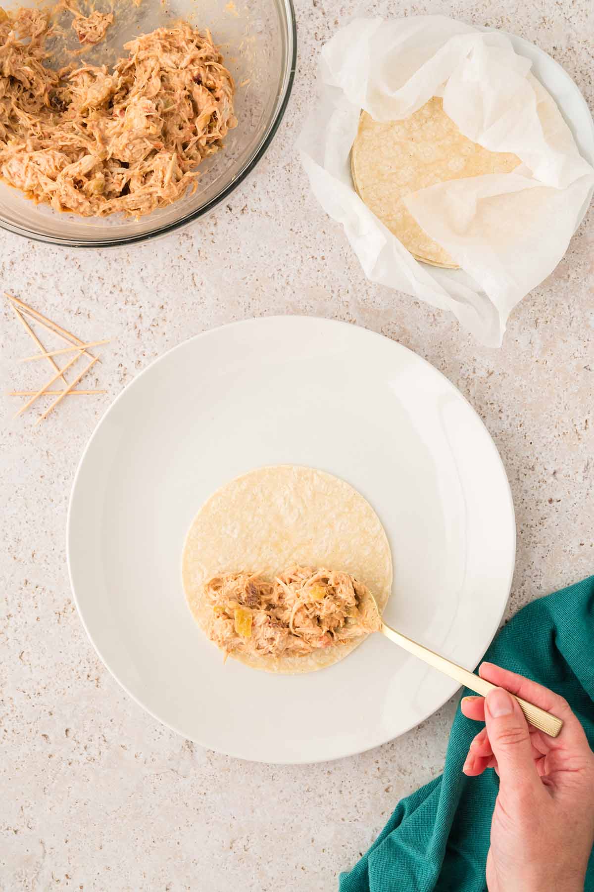 a hand placing shredded chicken mixture on a tortilla.