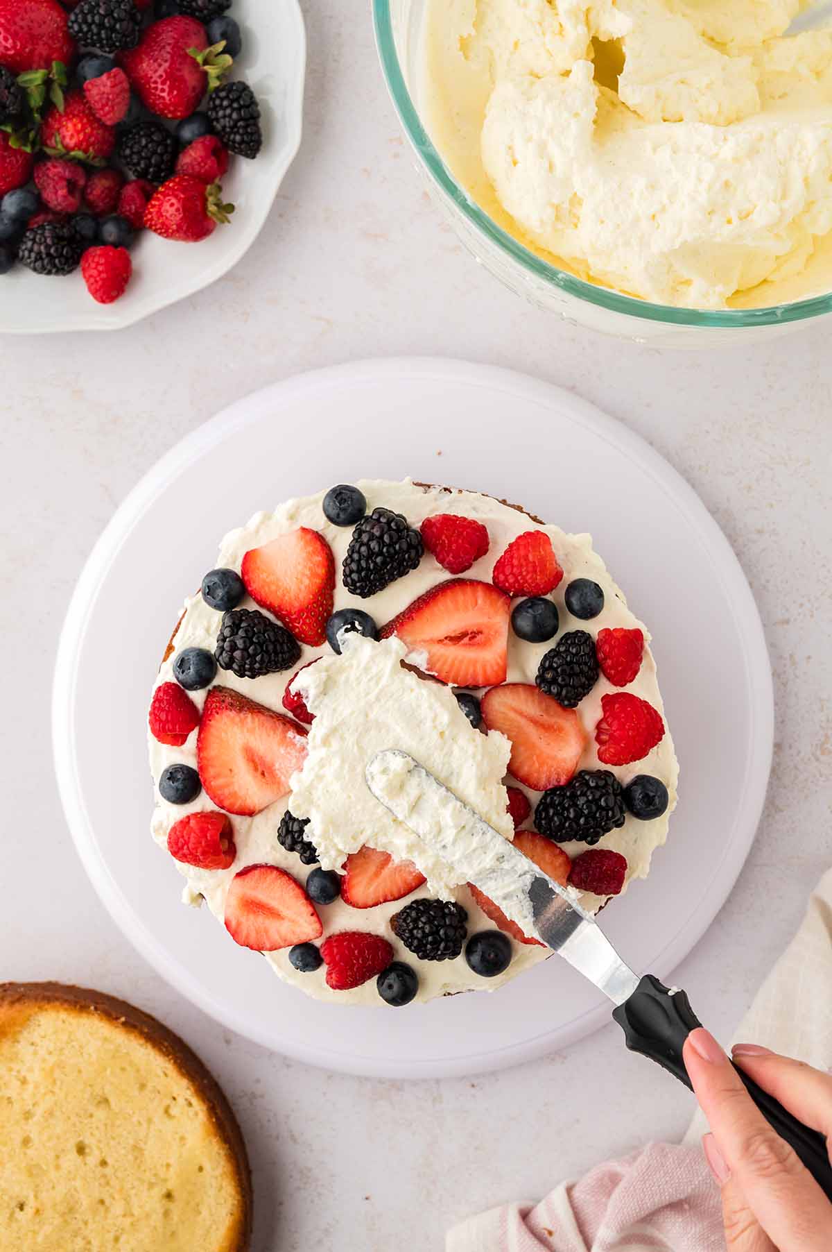 Cake layer being decorated with fruit and frosting.