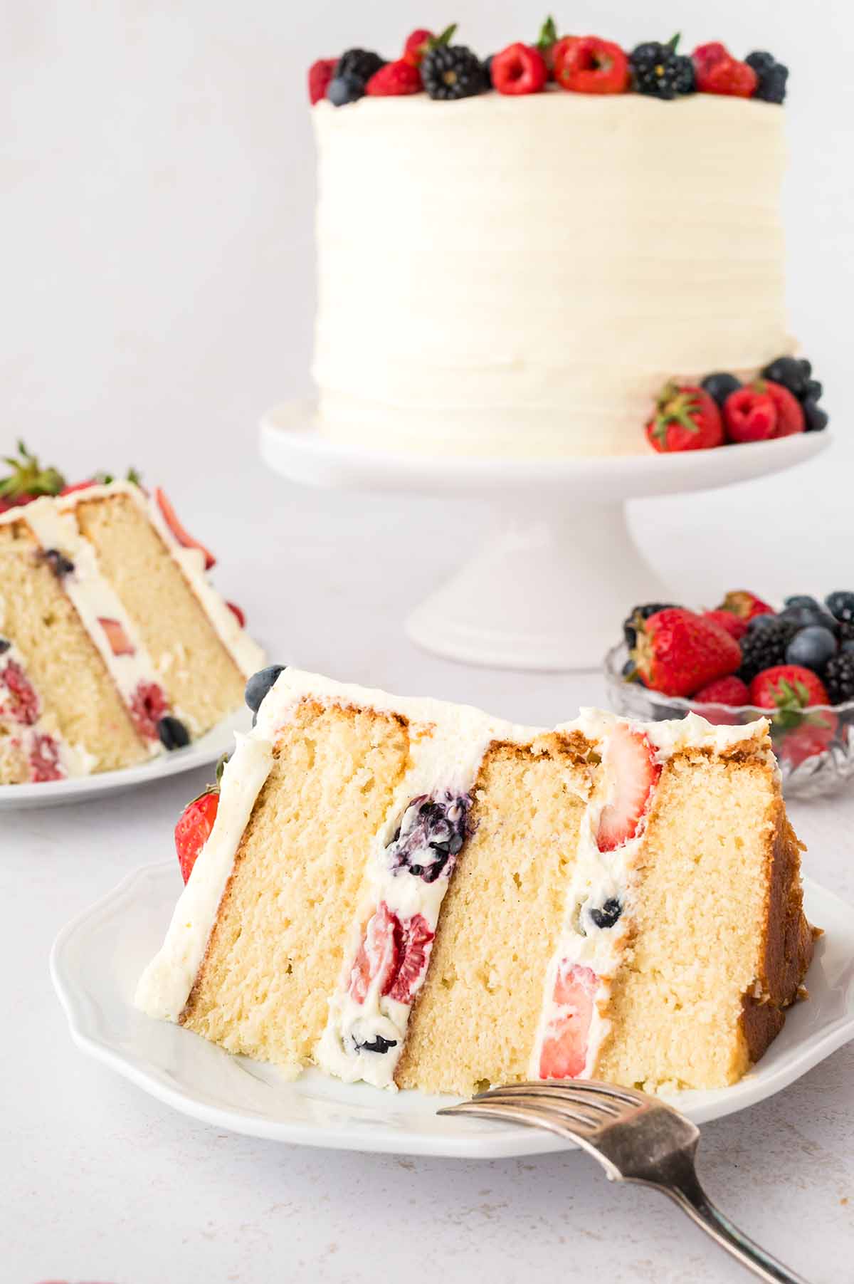 Two slices of cake on plates and an entire cake in the background.