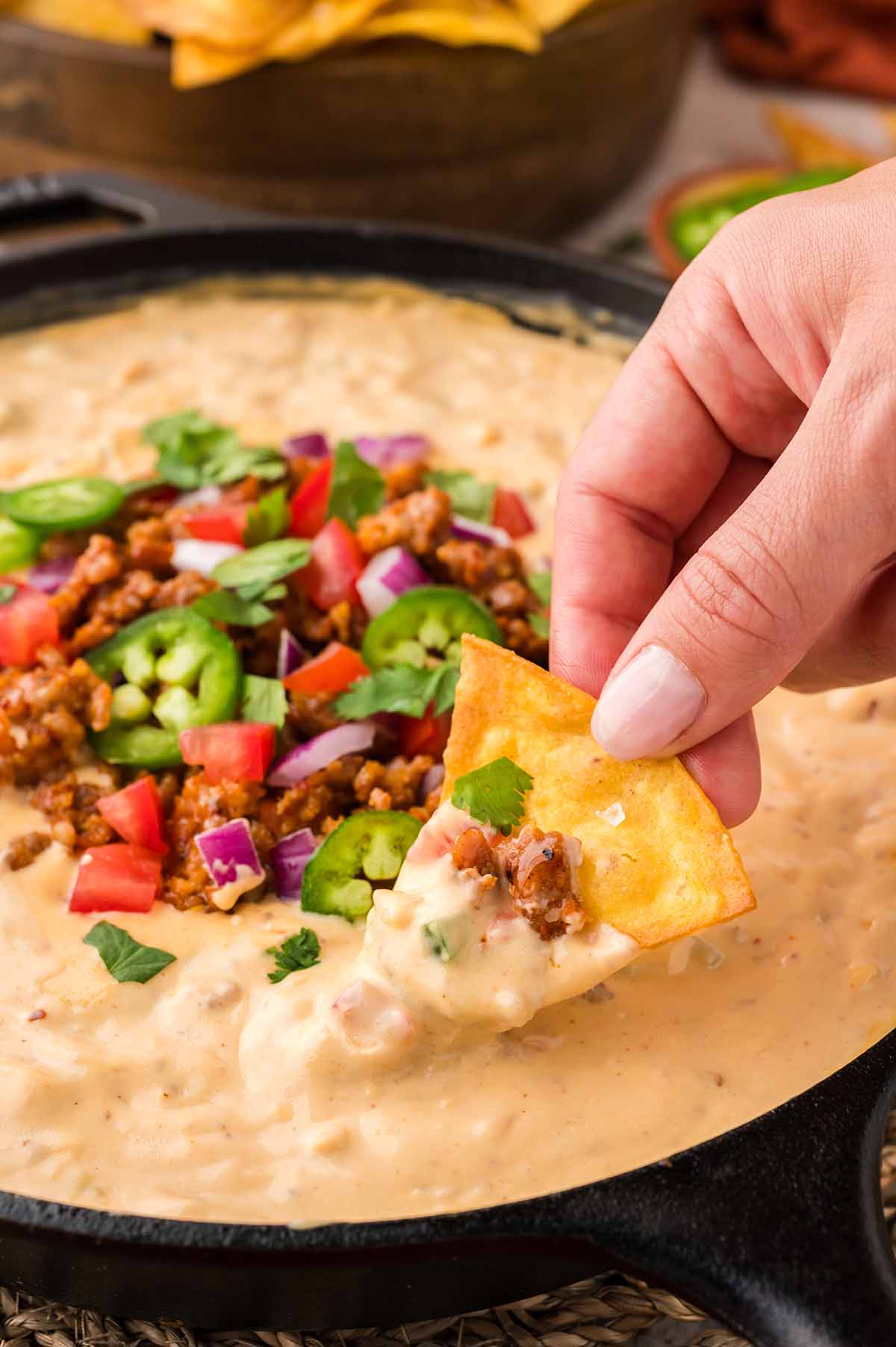 hand dipping tortilla chip into queso with chorizo.