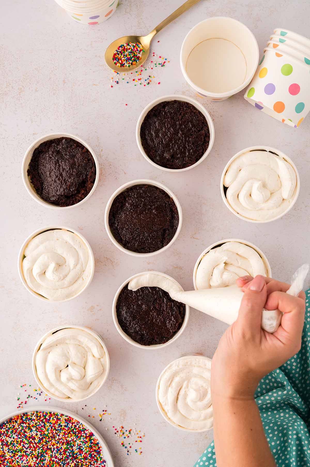 Hand piping frosting into cake cups with a piping bag.