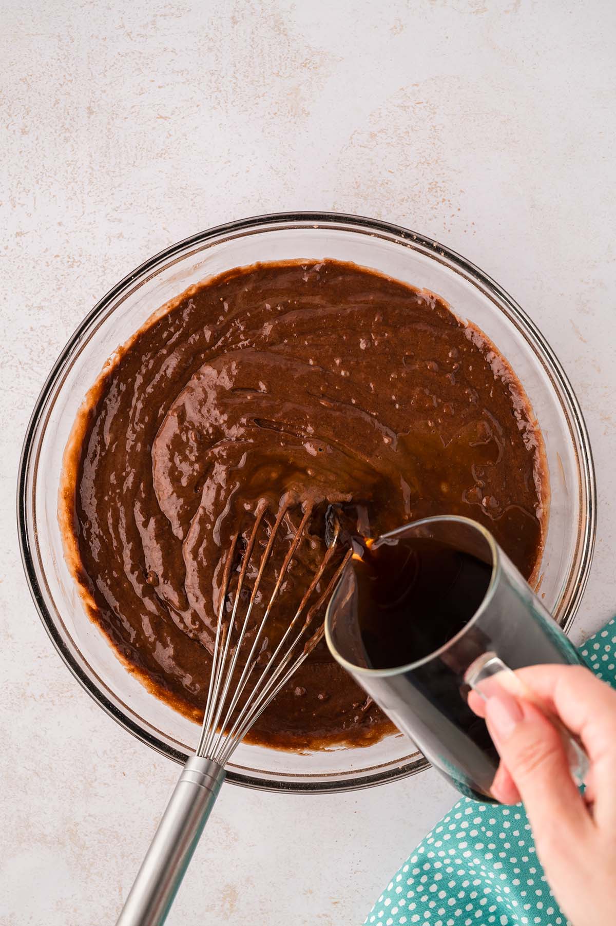 Coffee being poured into a bowl of chocolate cake batter.