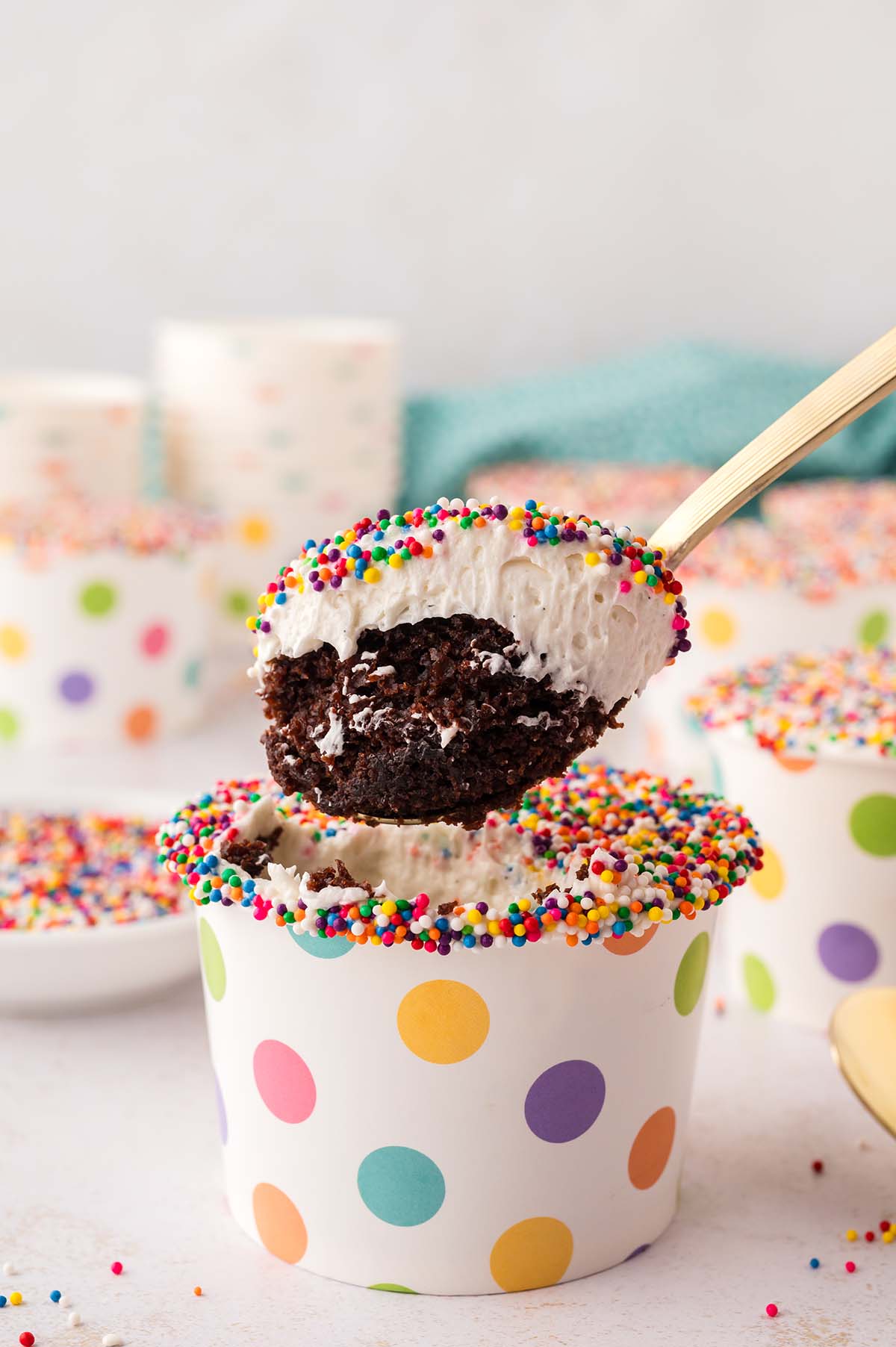 Spoon lifting a chocolate dot cake cup topped with vanilla frosting and rainbow sprinkles.