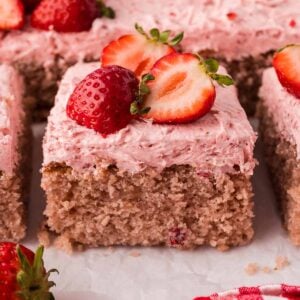 A slice of fresh strawberry cake with buttercream and fresh strawberries on top.