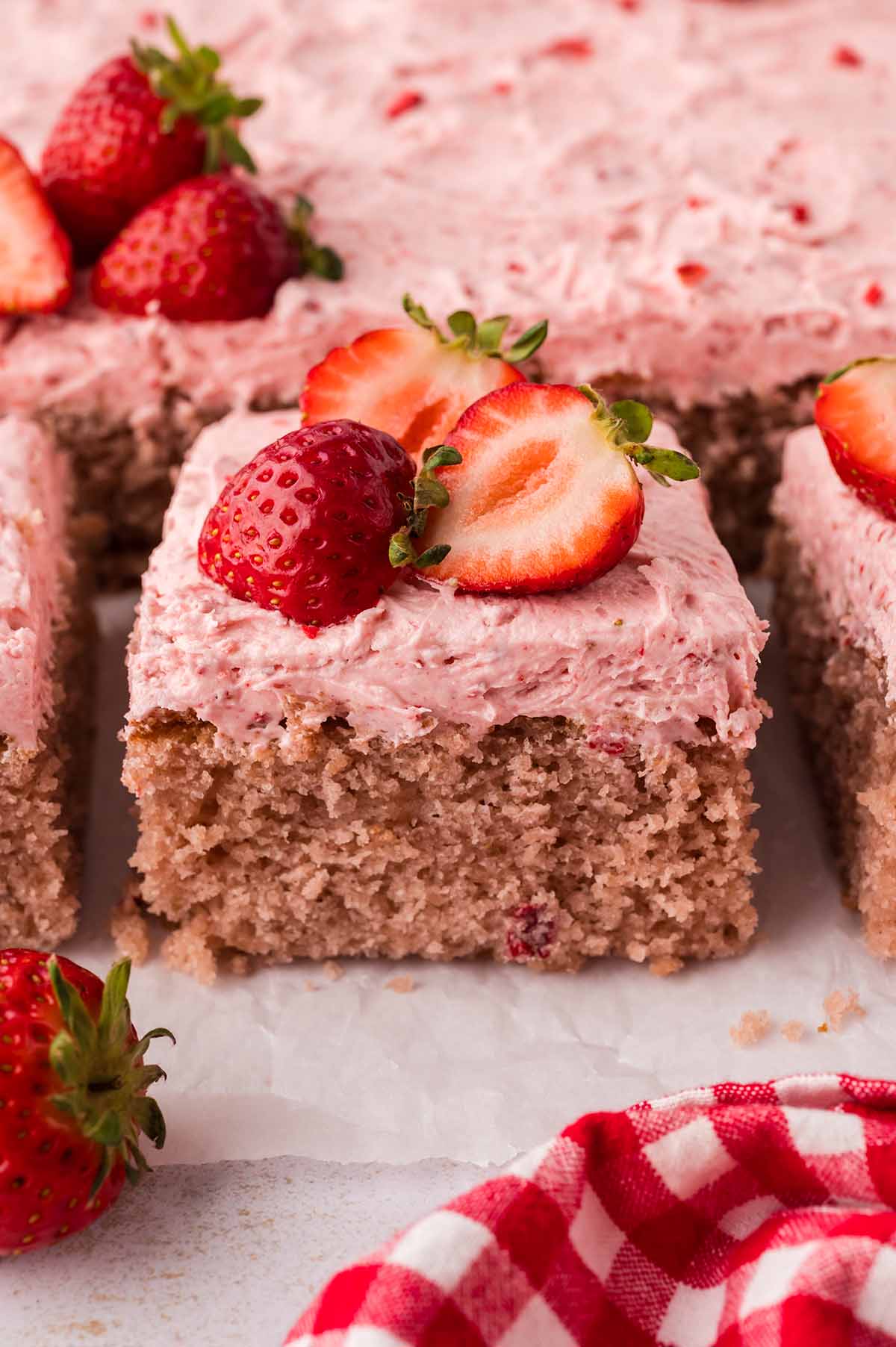 A slice of fresh strawberry cake with buttercream and fresh strawberries on top.
