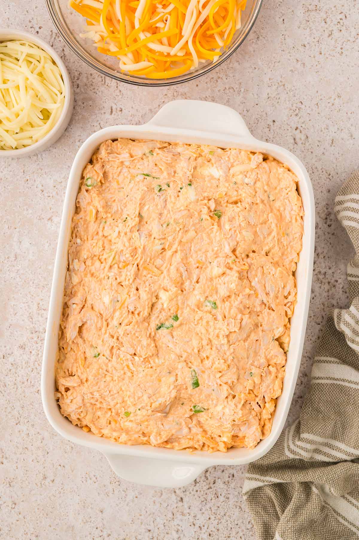 Buffalo chicken dip in a white baking dish with cheese on the side.