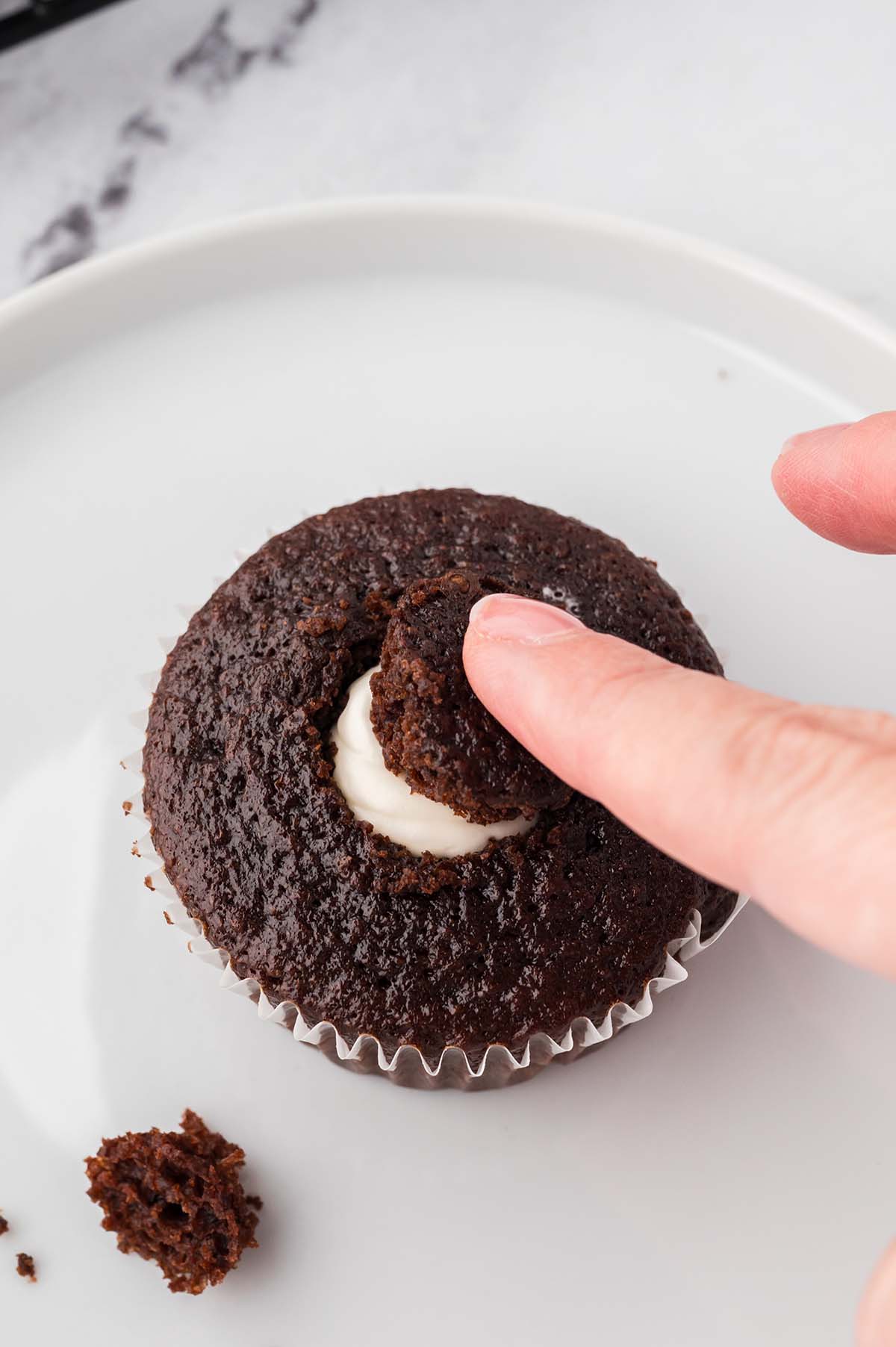 Placing the cut-out piece of cupcake back on top to cover the filled center.
