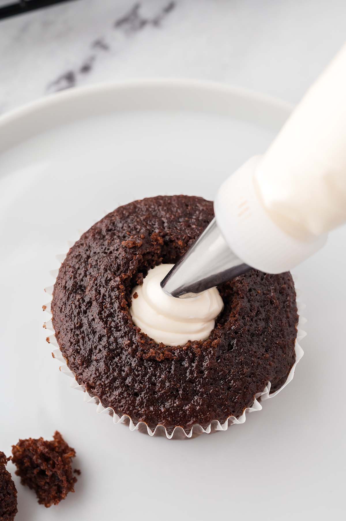a piping bag filling the center of a cupcake.