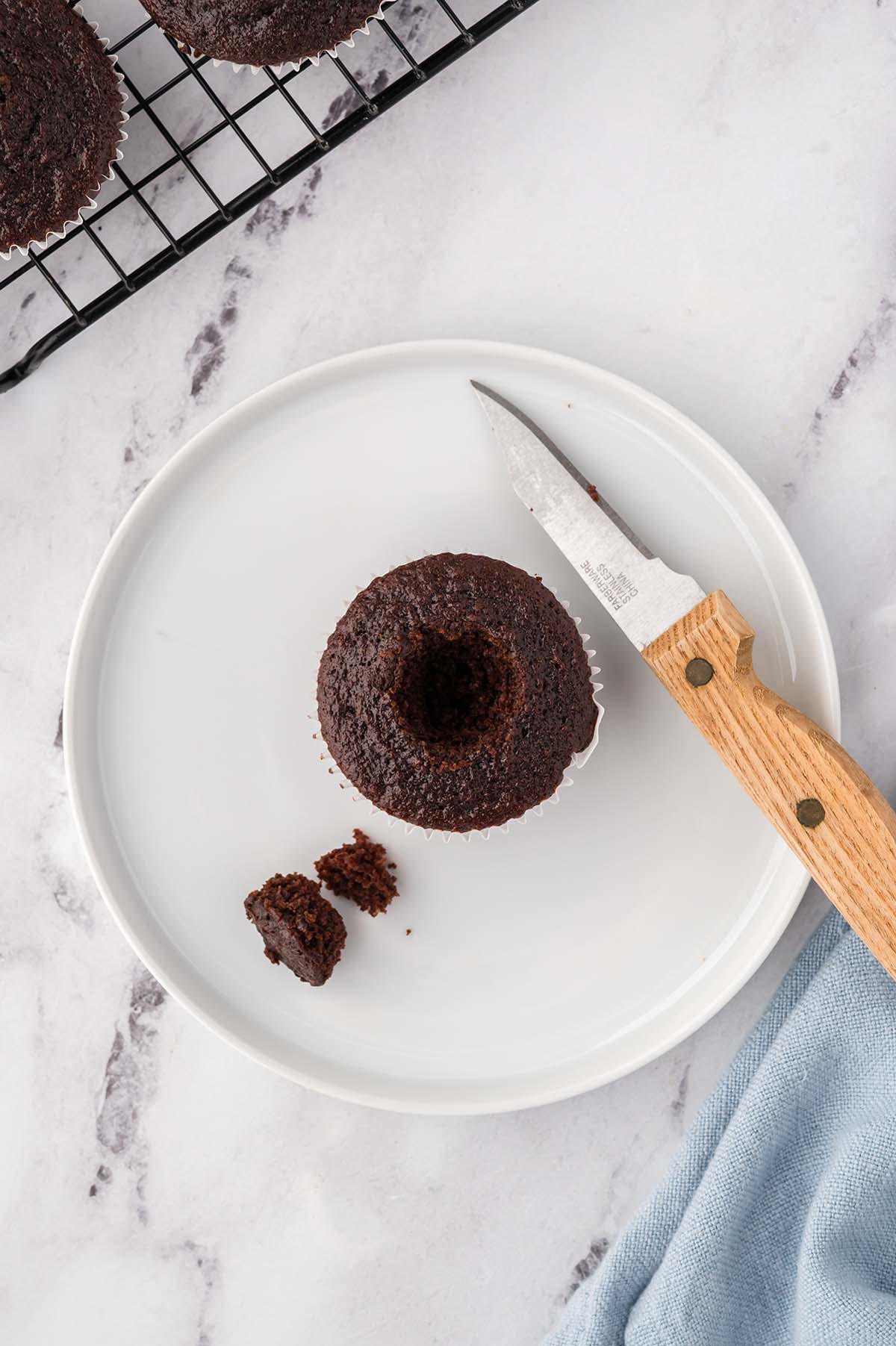 A chocolate cupcake with the center cut out, ready to be filled, with a knife on the side.