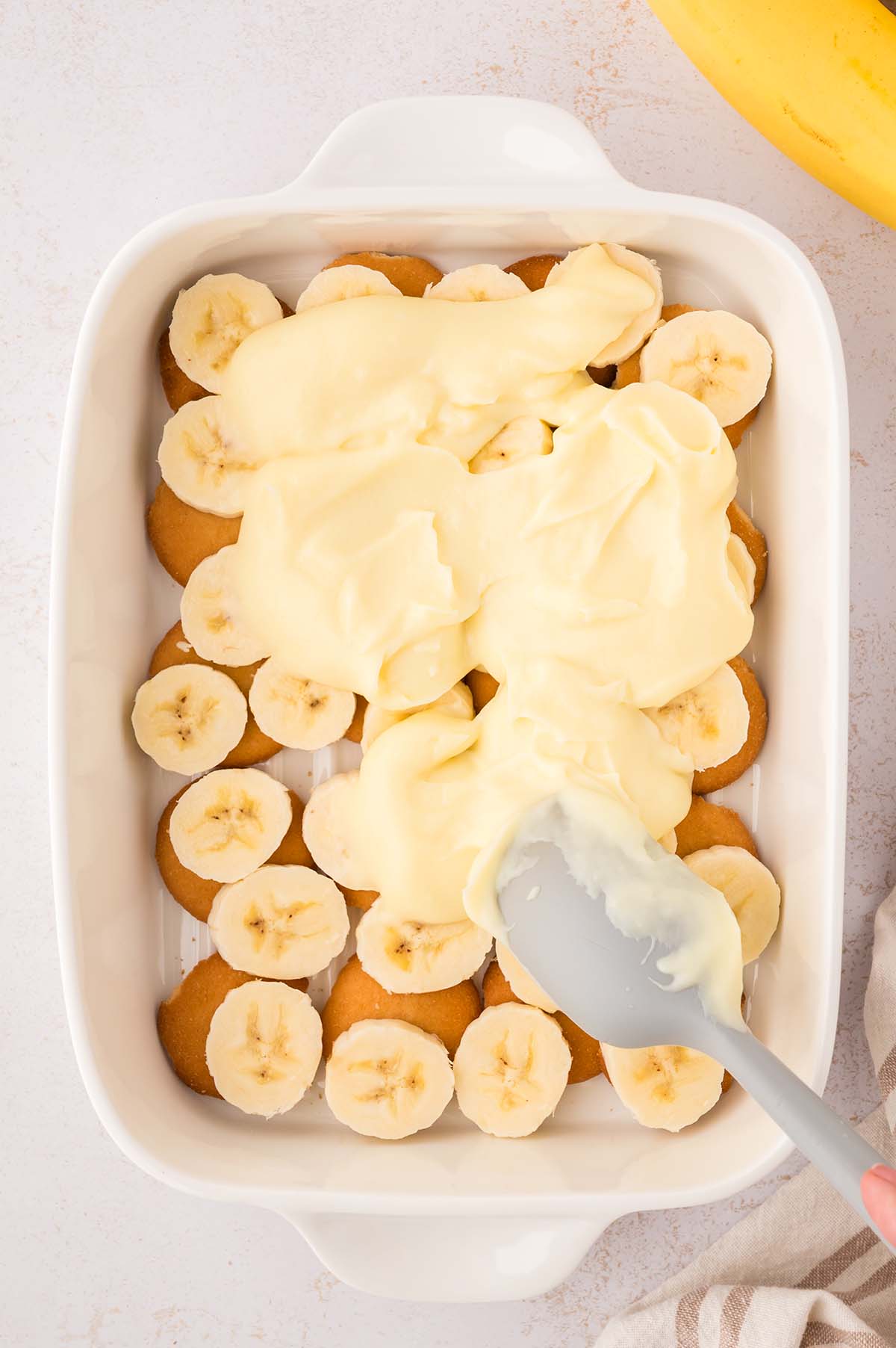 yellow pudding being spread on top of banana slices and vanilla wafers.