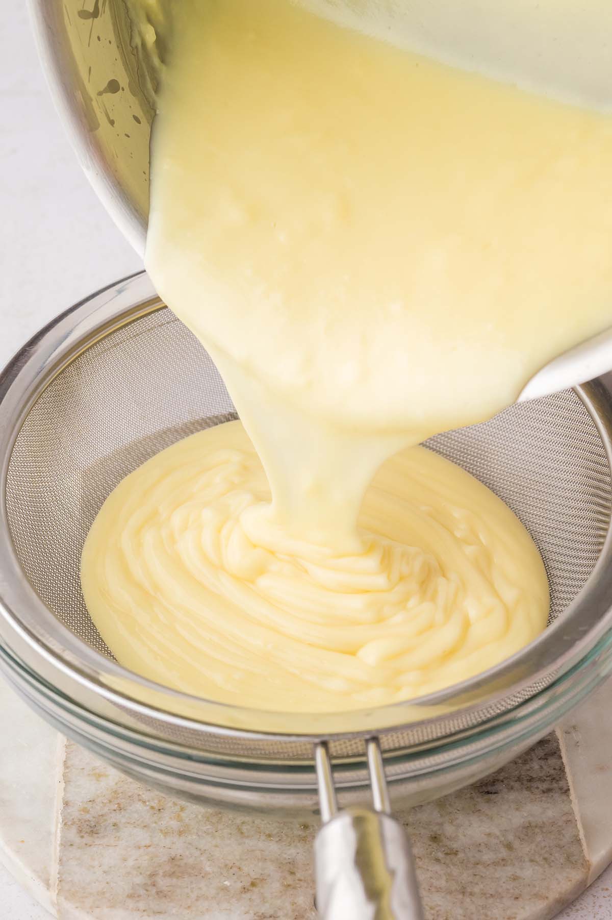 yellow custard going through a mesh sieve.