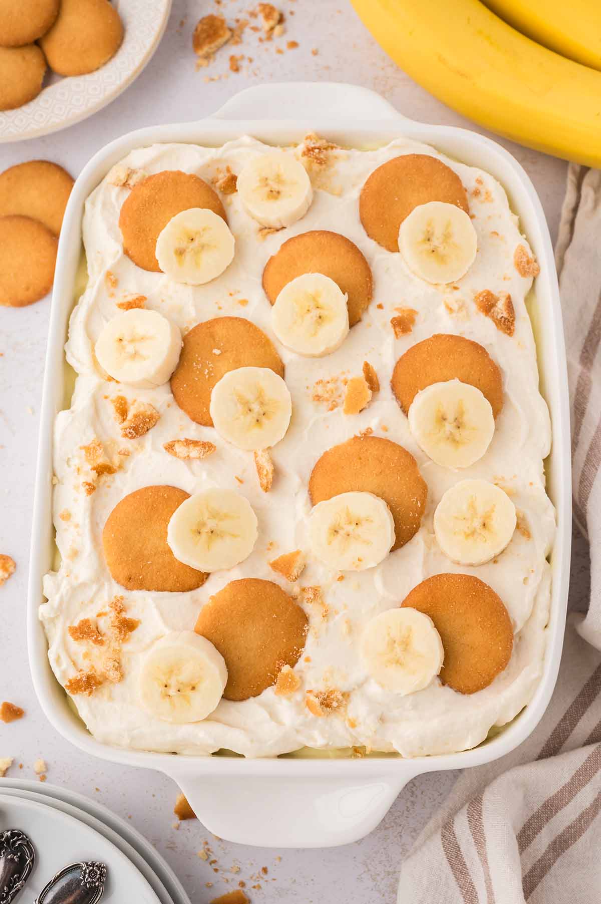 A white serving dish filled with creamy banana pudding, topped with fresh banana slices and vanilla wafers.