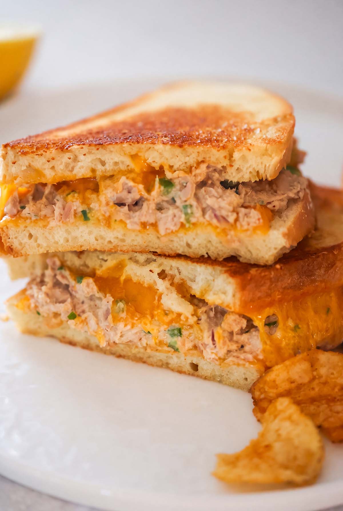 Two spicy tuna melt sandwiches stacked on top of each other and chips on the side.