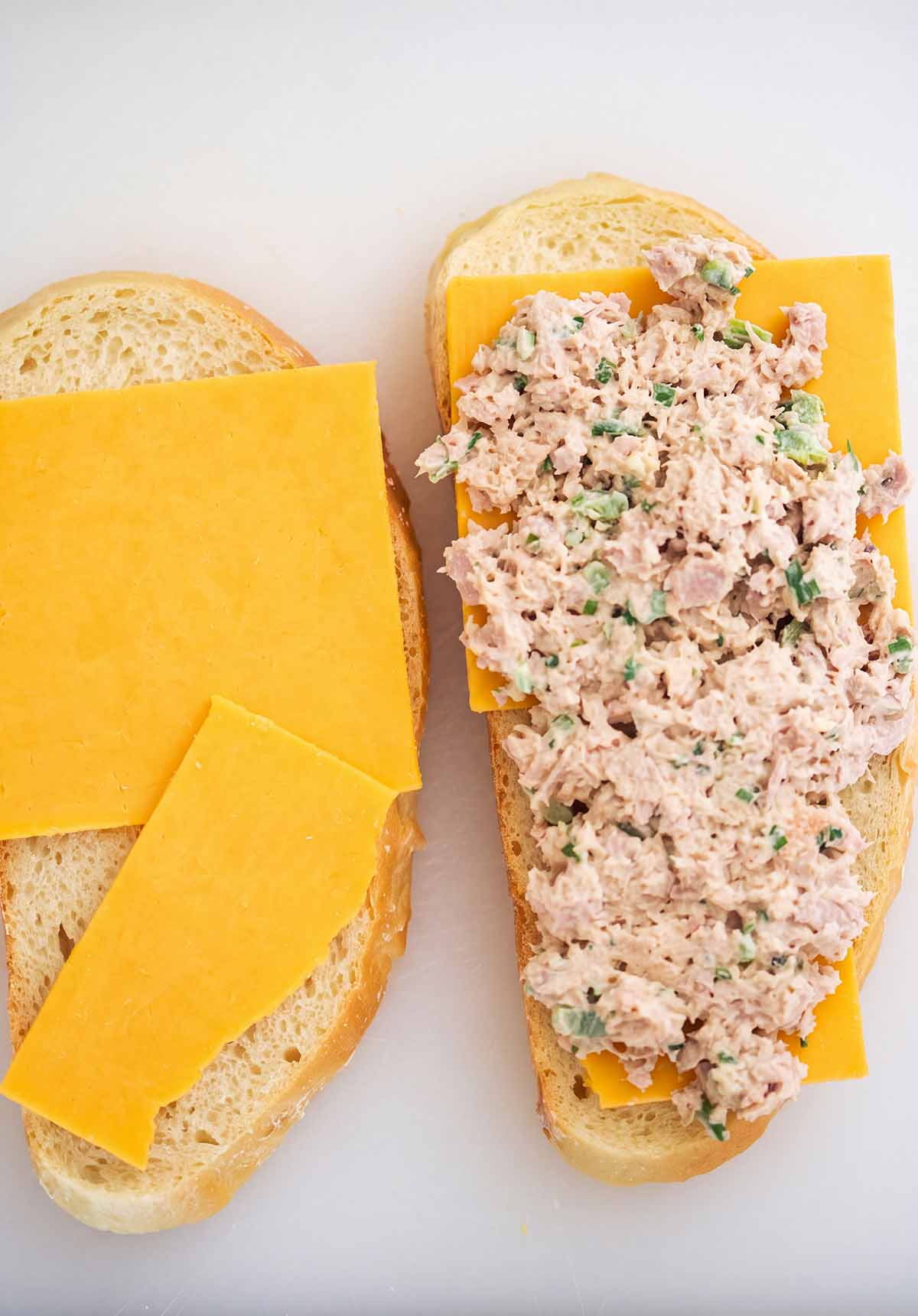 two slices of bread with cheddar cheese and tuna salad on one slice.