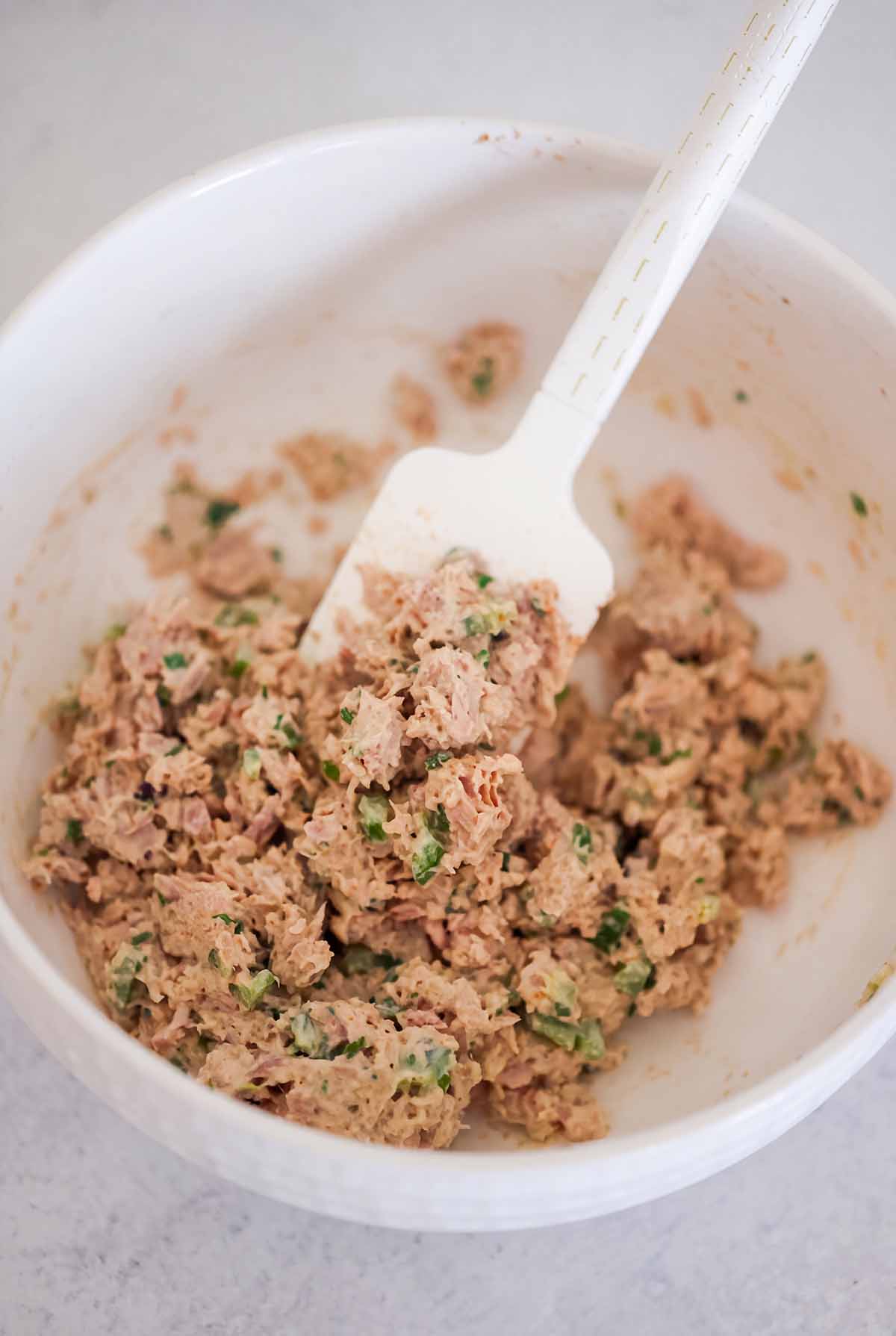 Tuna salad and a rubber spatula in a white bowl.