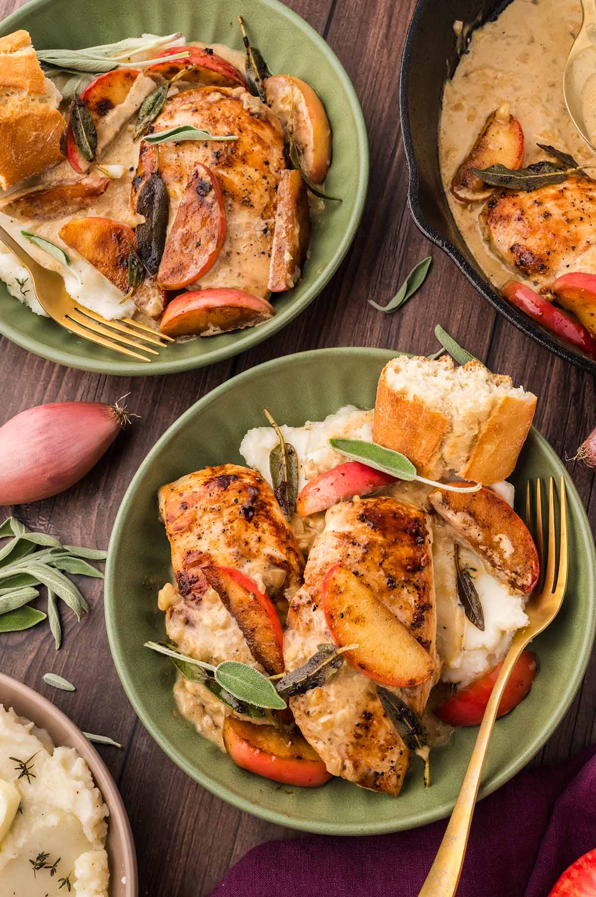 two green plates filled with chicken, apples, sage, mashed potatoes, and bread.