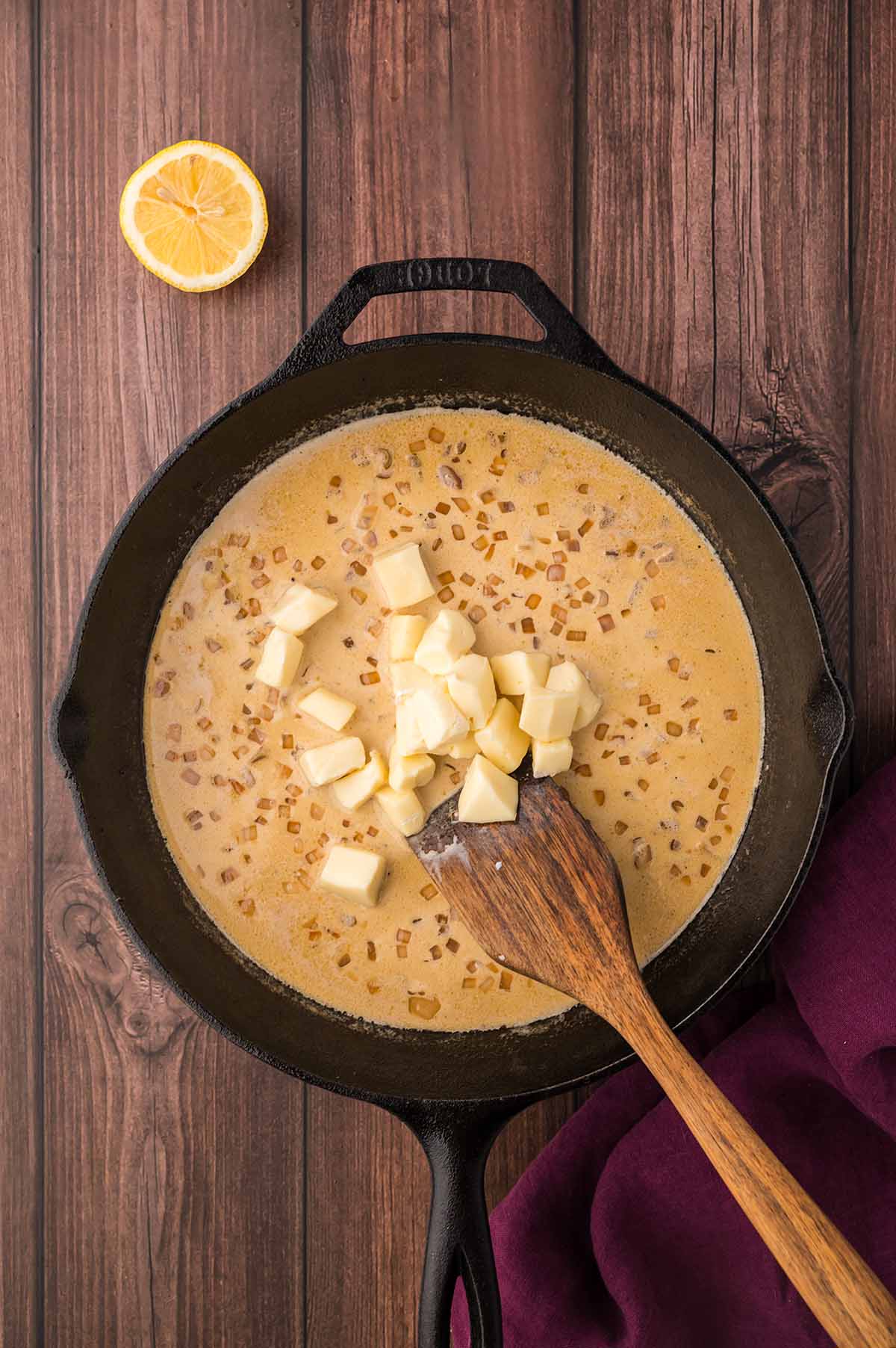brie, shallots, cream, and a wooden spoon in a skillet with lemon on the side.