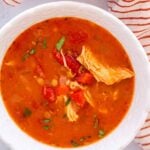 chicken tomato lentil soup in a white bowl with a towel on the side.