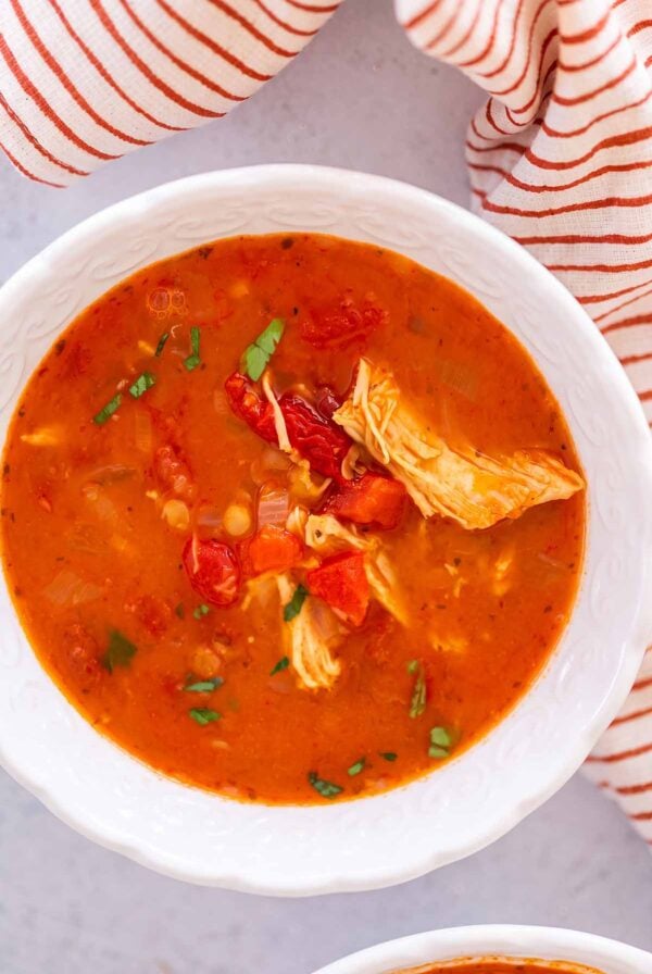 chicken tomato lentil soup in a white bowl with a towel on the side.