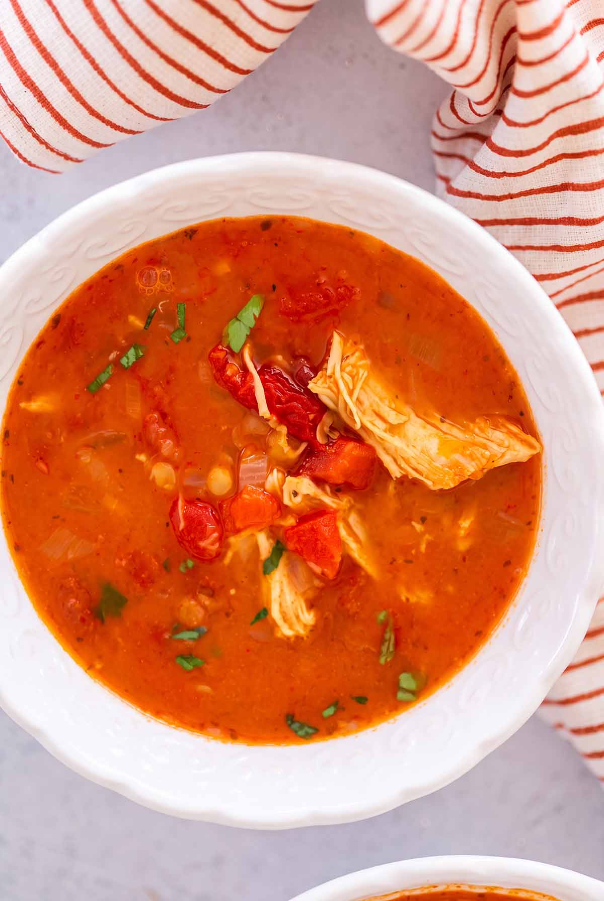 chicken tomato lentil soup in a white bowl with a towel on the side.