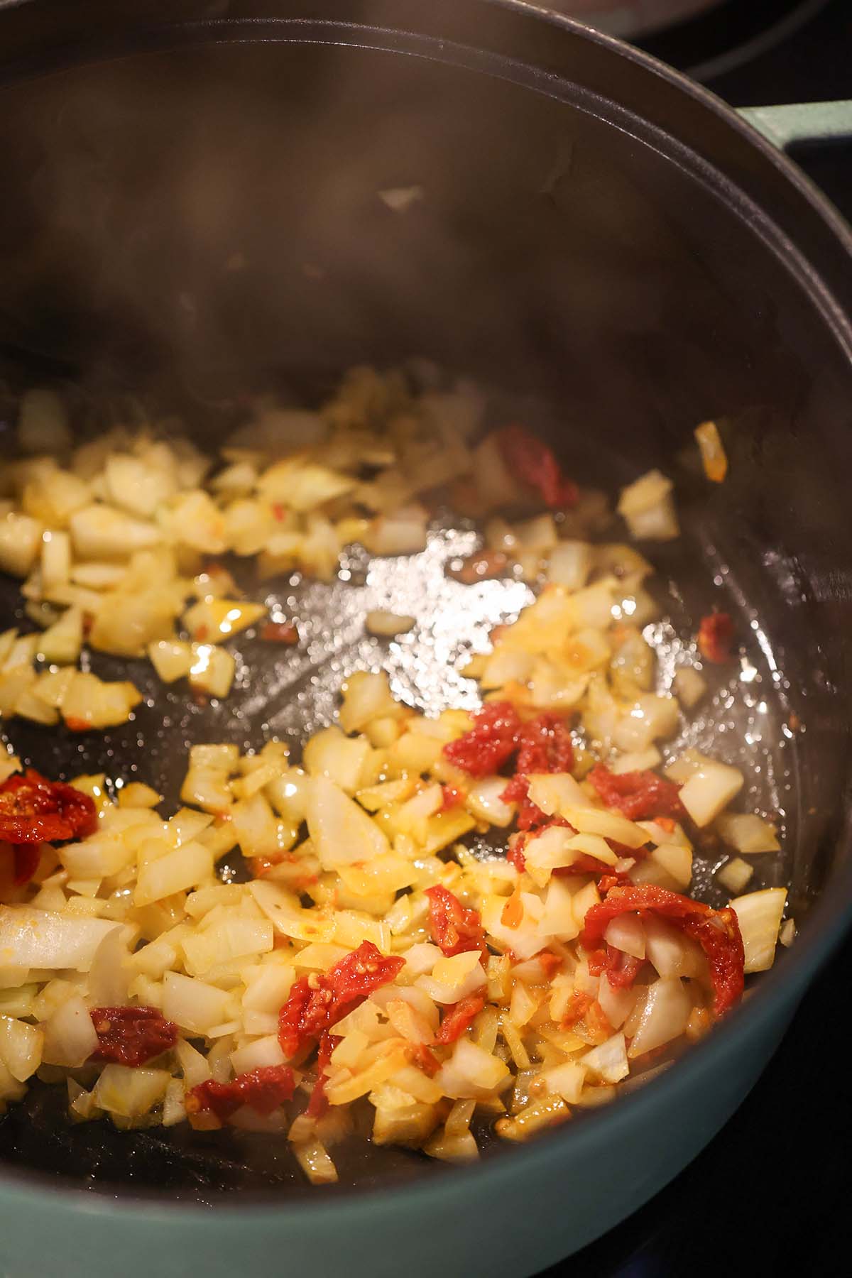 onions and sun dried tomatoes sautéing in a pot.
