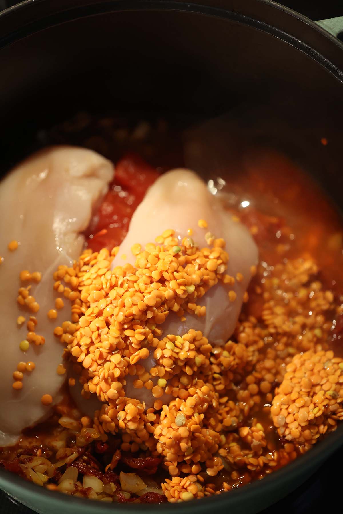 raw chicken breasts, raw lentils, and chicken stock in a pot.