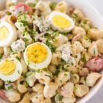 Cobb pasta salad in a white bowl with sliced eggs and chives on top.