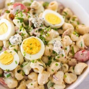 Cobb pasta salad in a white bowl with sliced eggs and chives on top.