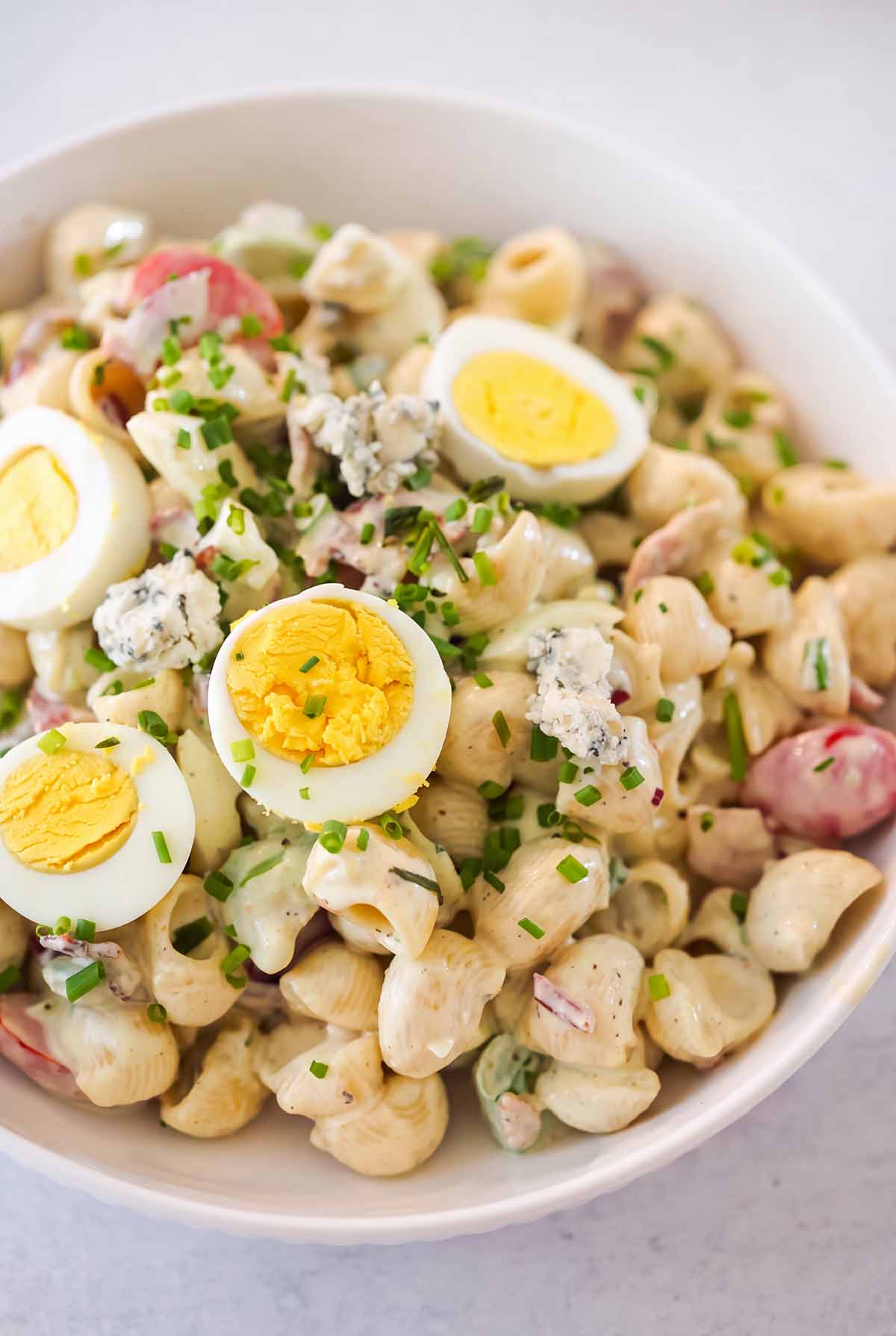 Cobb pasta salad in a white bowl with sliced eggs and chives on top.