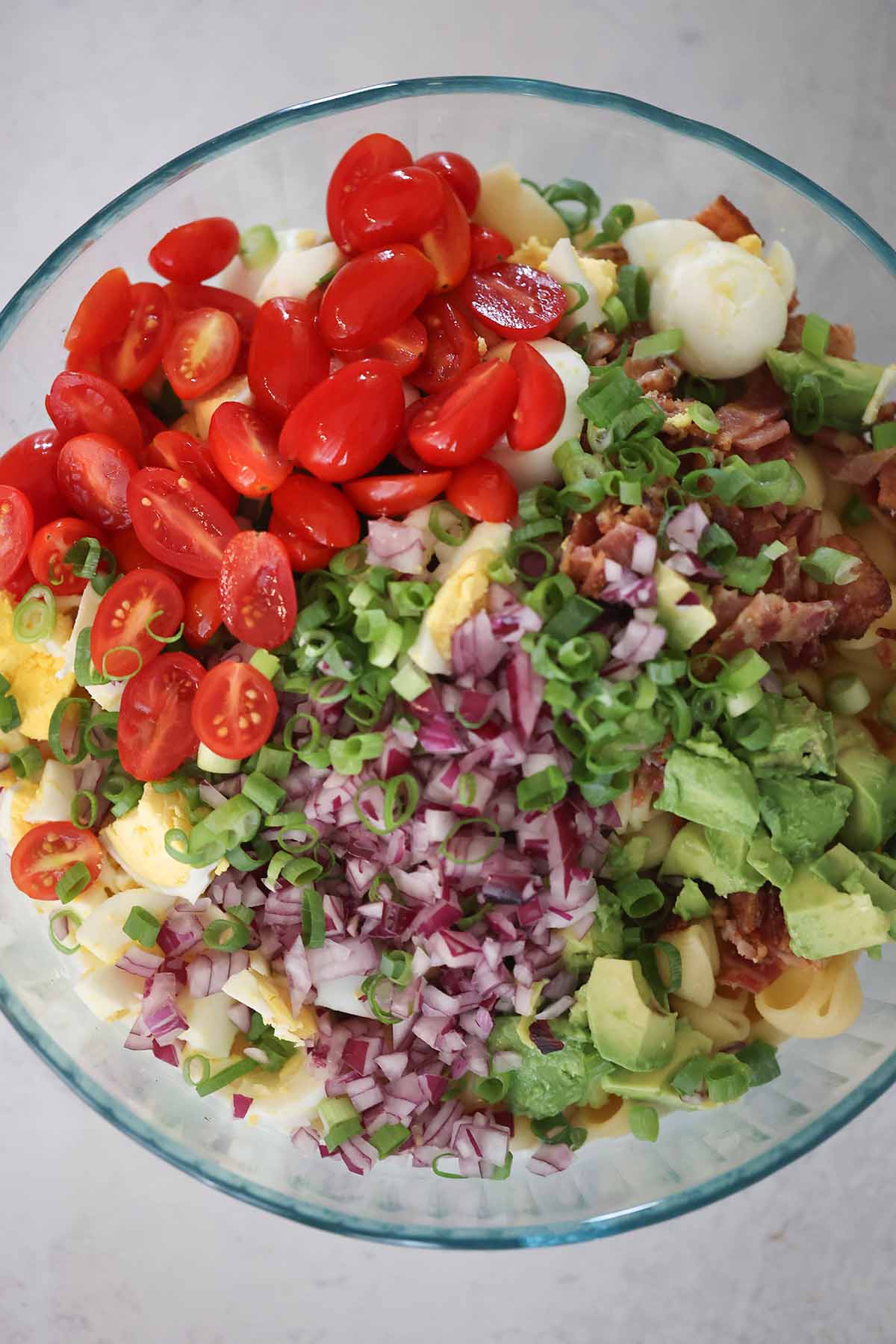 Tomatoes, avocado, onions, bacon, eggs, and pasta in a bowl.