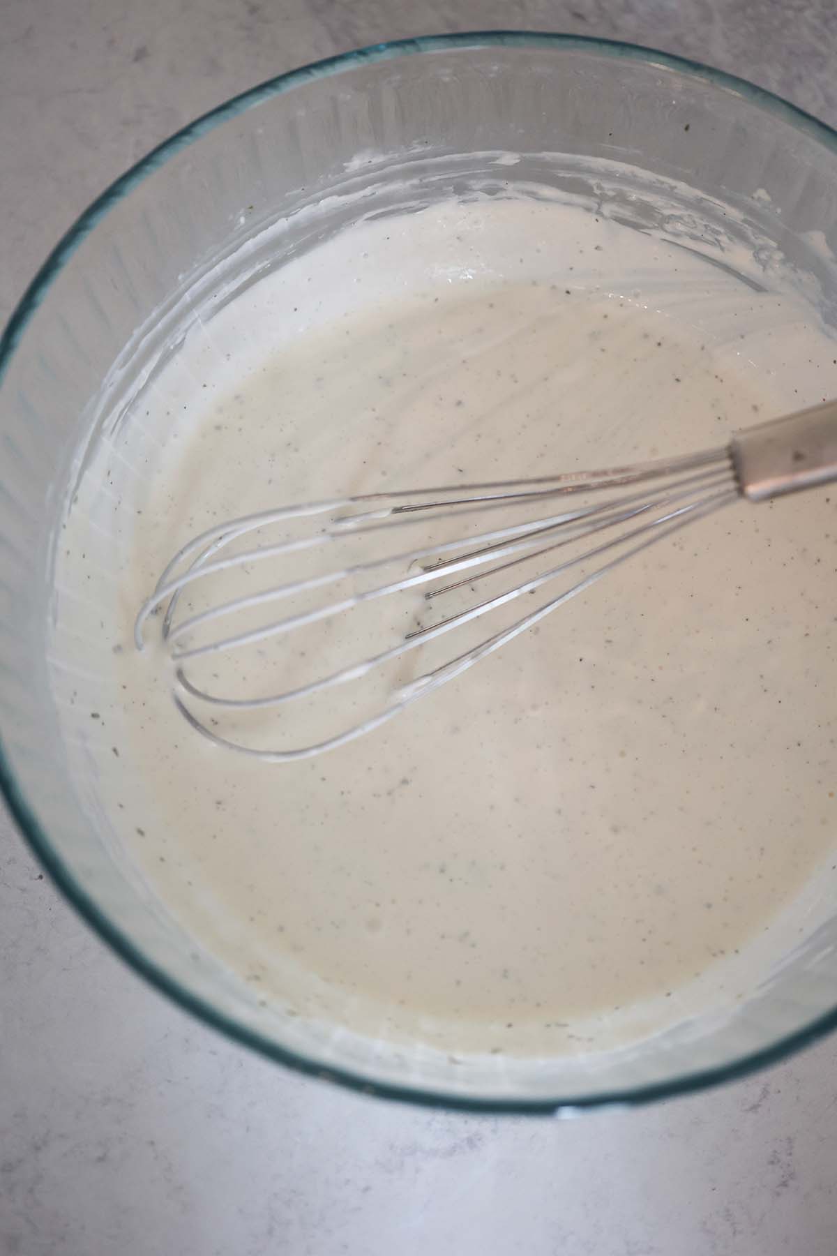 dressing in a glass bowl with a whisk.