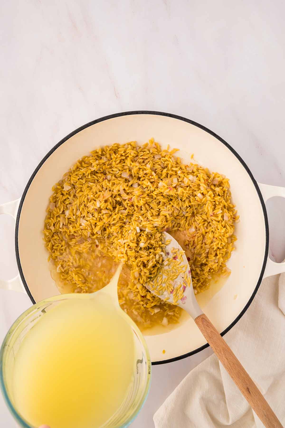chicken stock being poured into a skillet with orzo.