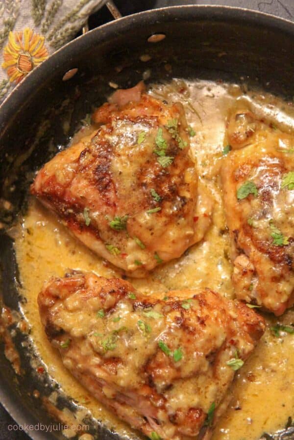 three smothered chicken thighs with a cream sauce in a skillet.