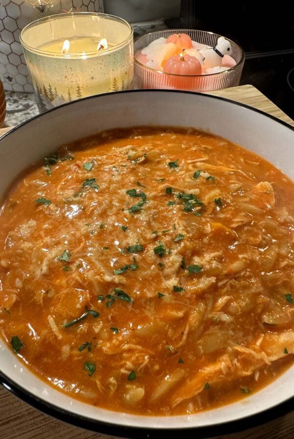 a spicy tomato chicken orzo soup with candles in the background.