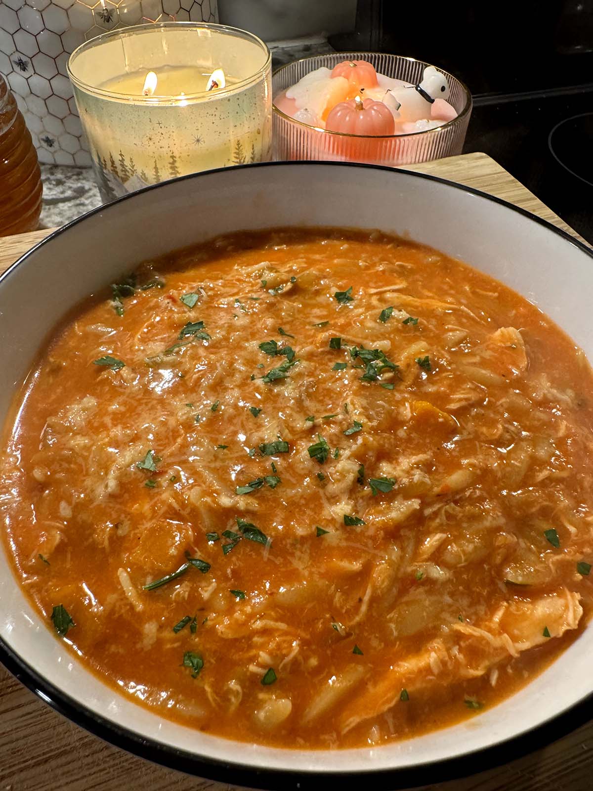 a spicy tomato chicken orzo soup with candles in the background.