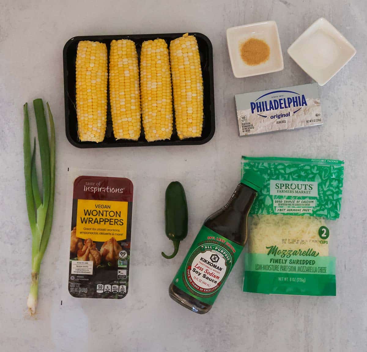 corn, cheese, garlic, cheese, jalapeño pepper, soy sauce, wonton wrappers, and scallions on a gray surface.