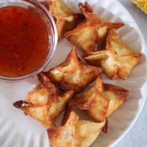 seven corn Rangoons on a white plate with sweet chili sauce on the side.