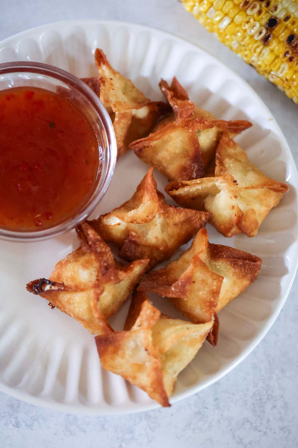 seven corn Rangoons on a white plate with sweet chili sauce on the side.