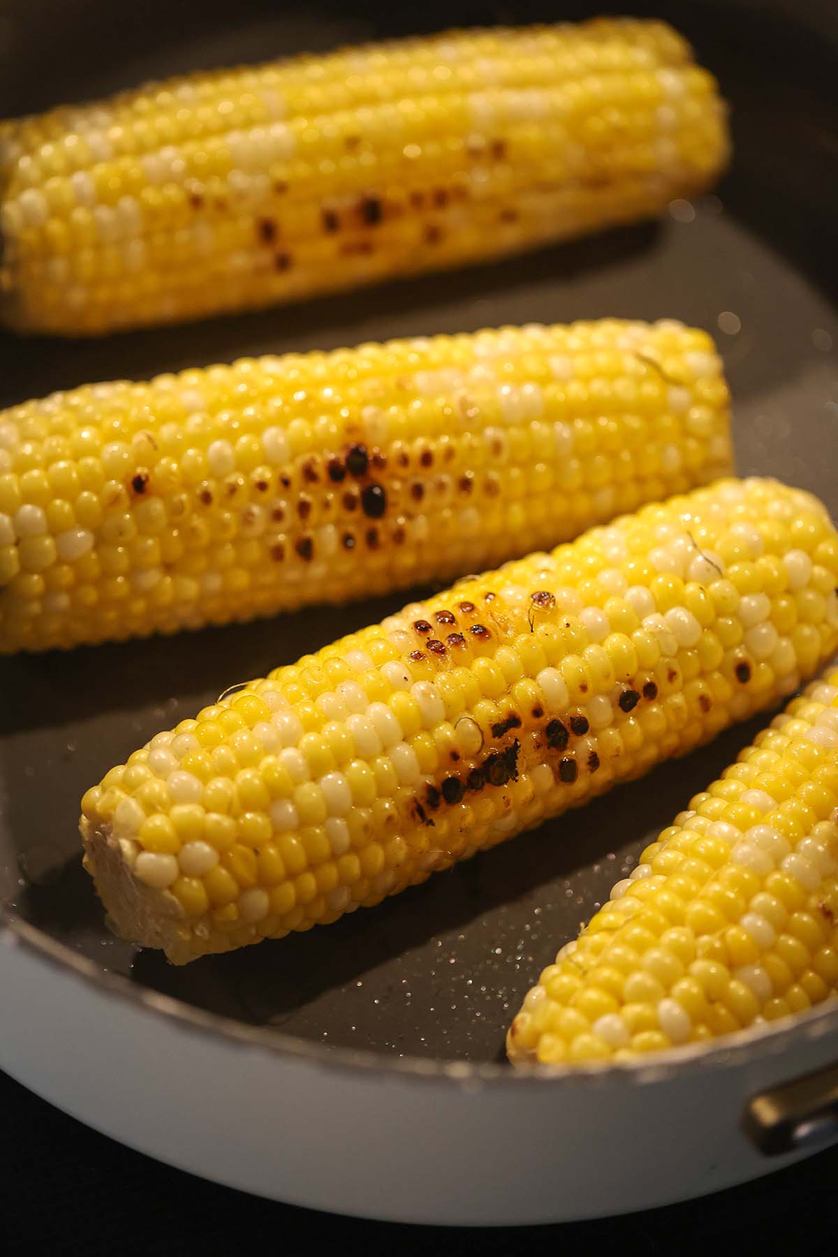 three ears of corn cooking on the stove.