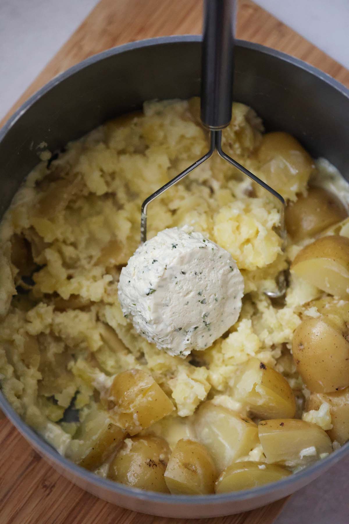 Cubed potatoes with a big chunk of Boursin cheese and a potato masher.