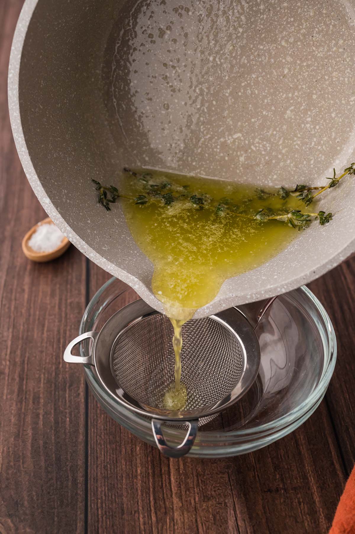 Straining the thyme-infused melted butter through a fine-mesh sieve.
