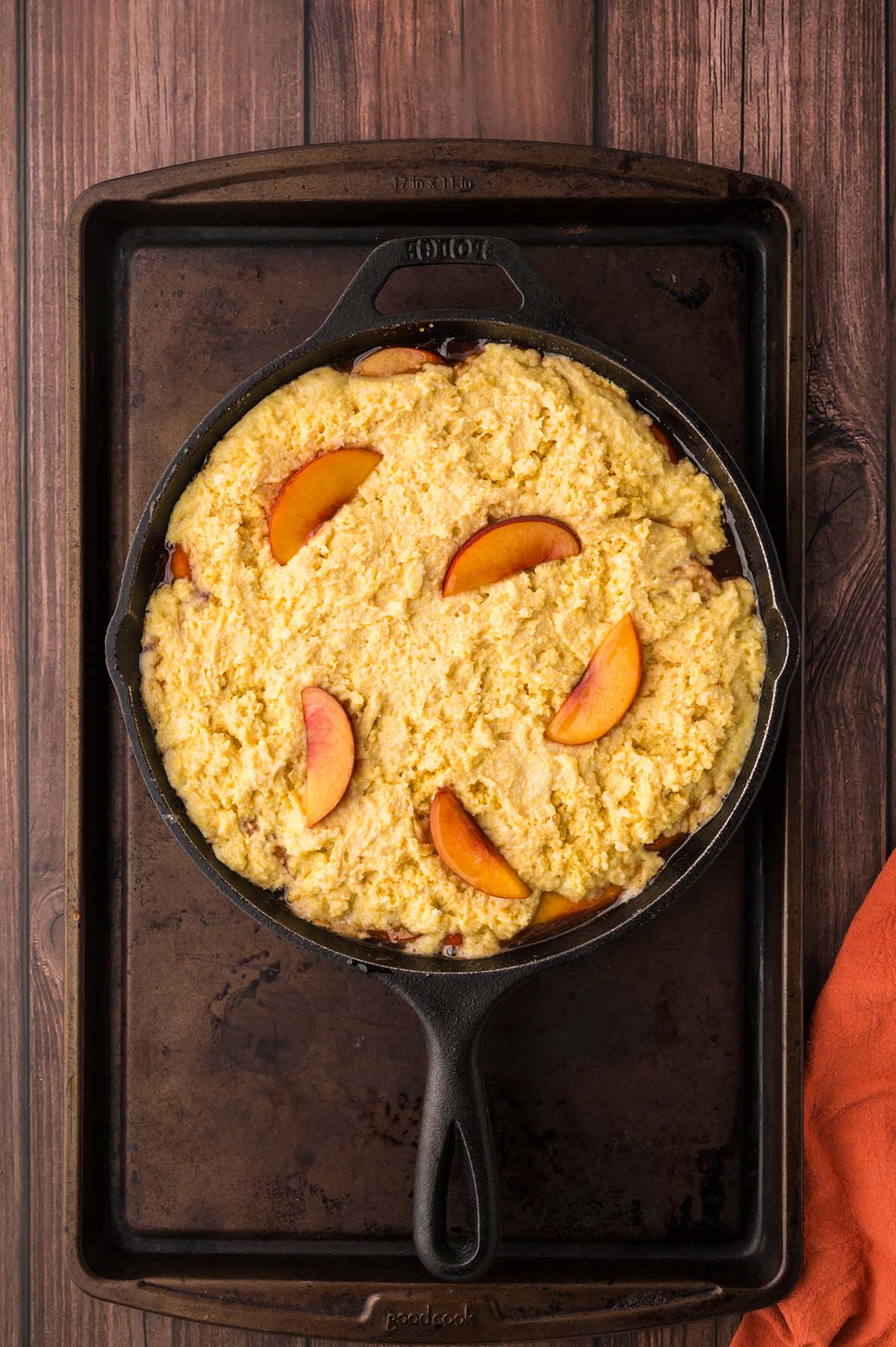 cornbread batter in an iron skillet with fresh peaches on top.