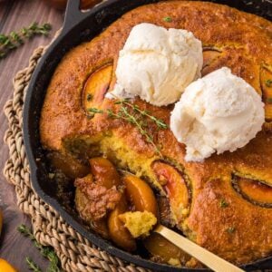cornbread peach cobbler with two scoops of vanilla ice cream on top.