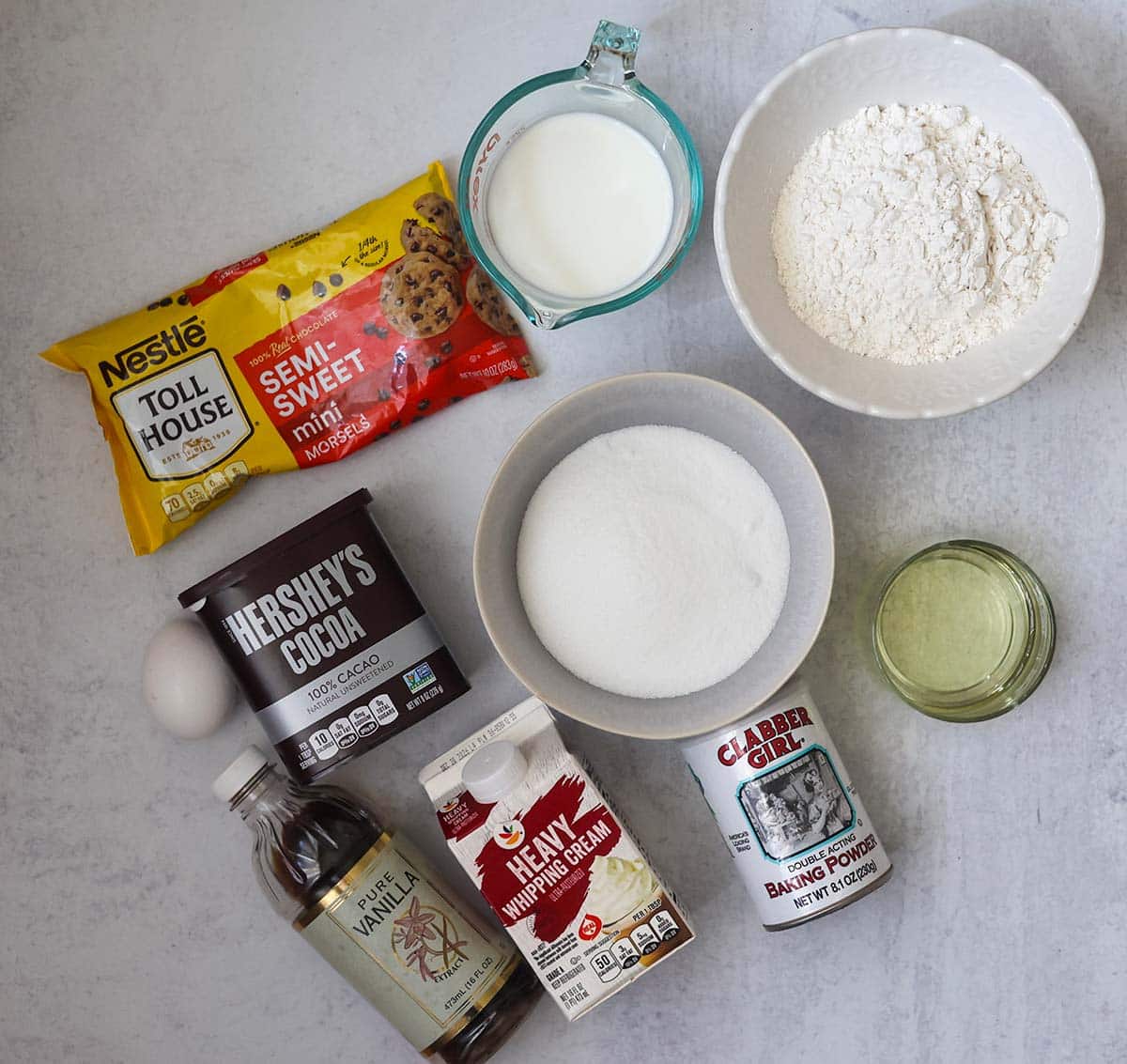 sugar, flour, oil, heavy cream, baking powder, cocoa powder, chocolate chips, milk, vanilla extract, and an egg.