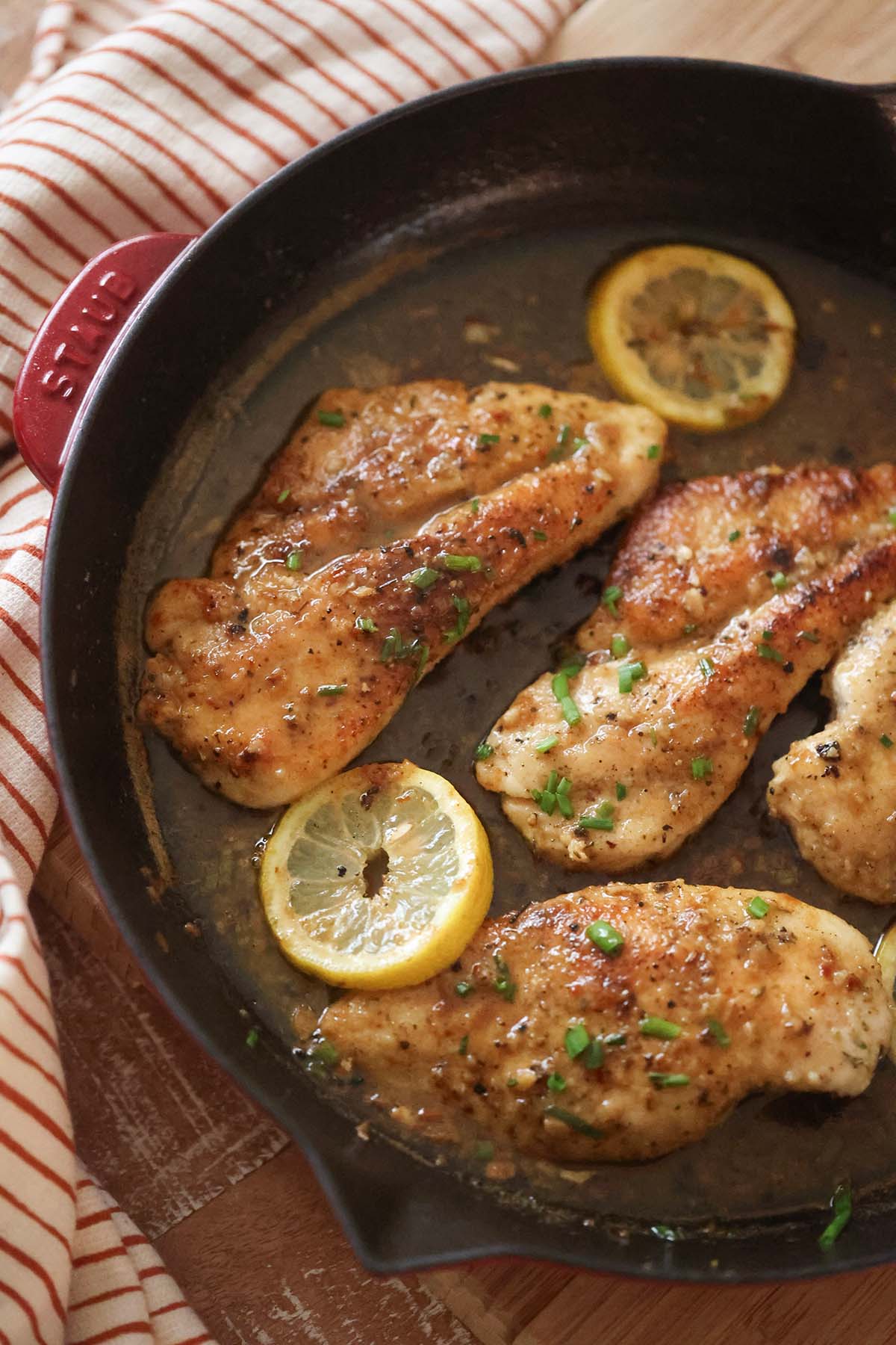chicken breasts with sauce, lemon slices, and chives on top.