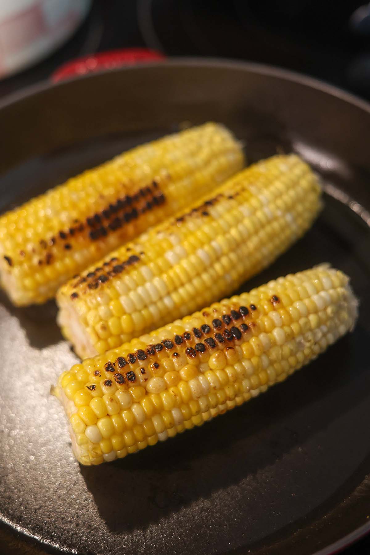 corn on the cob cooking in a cast iron skillet.